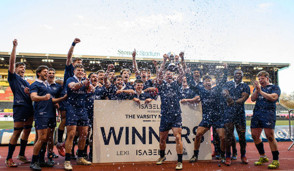 Oxford’s Men’s Blues celebrate their Varsity victory at StoneX Stadium, lifting the trophy behind a winners’ board as water sprays into the air. The team, dressed in navy kits, cheer with arms raised on the pitch following their win over Cambridge.